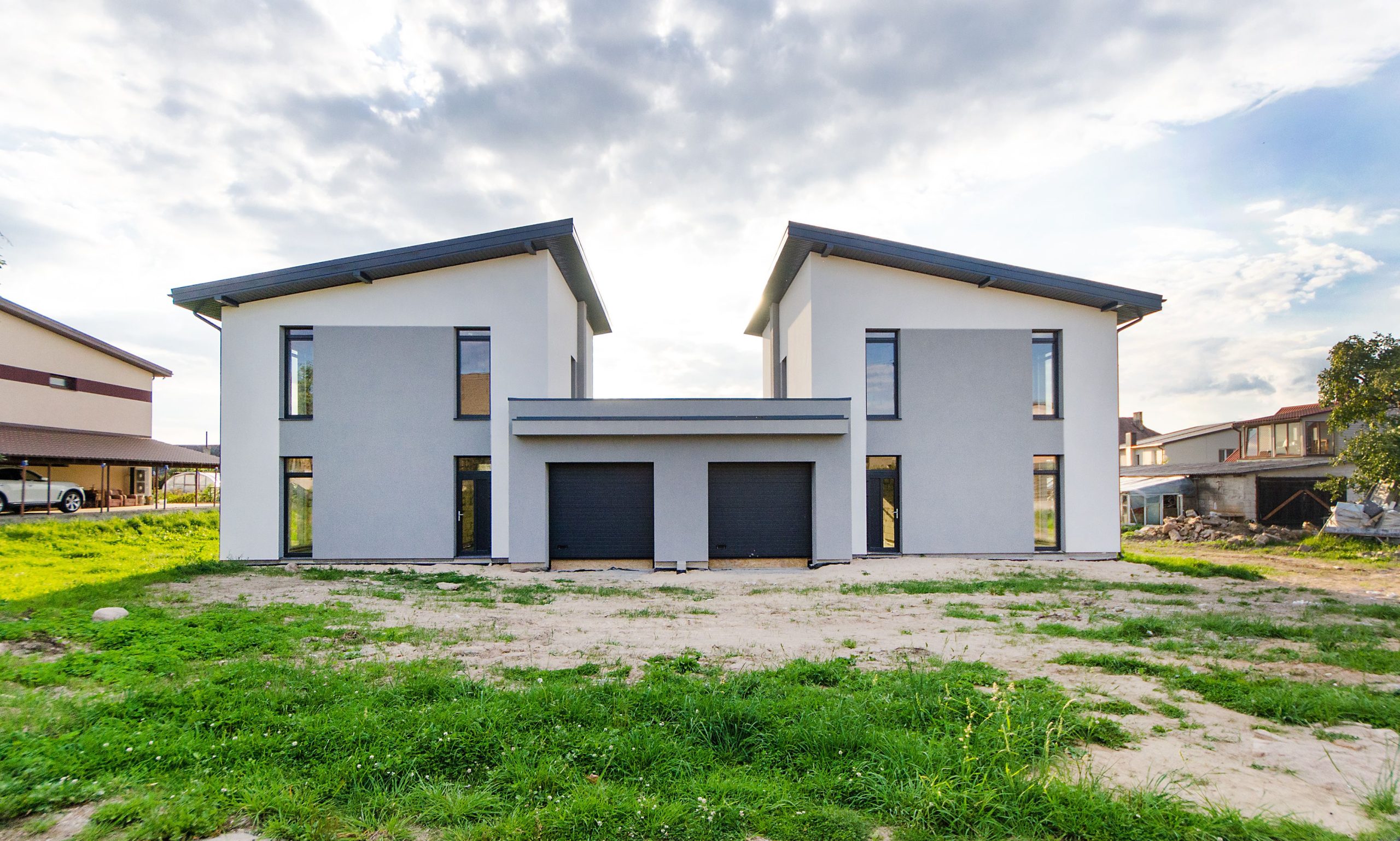 Front view of twin modern houses with a symmetrical architectural design under a cloudy sky.